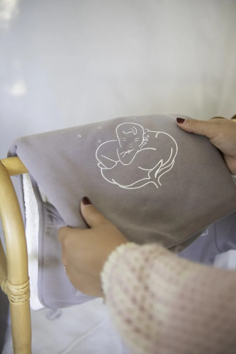 Couverture bébé bio gris violine pliée, tenue par une maman