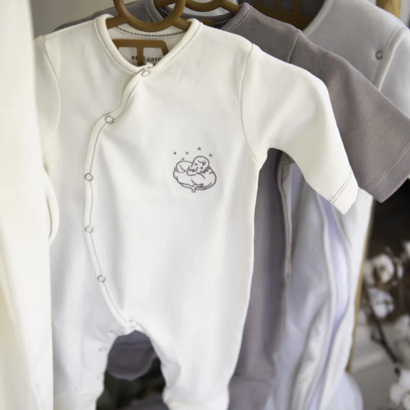 Grenouillères bébé bio écrue et grise suspendues sur des cintres