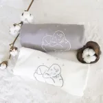 Couvertures bébé en coton bio écrue et grise roulées, avec un doudou