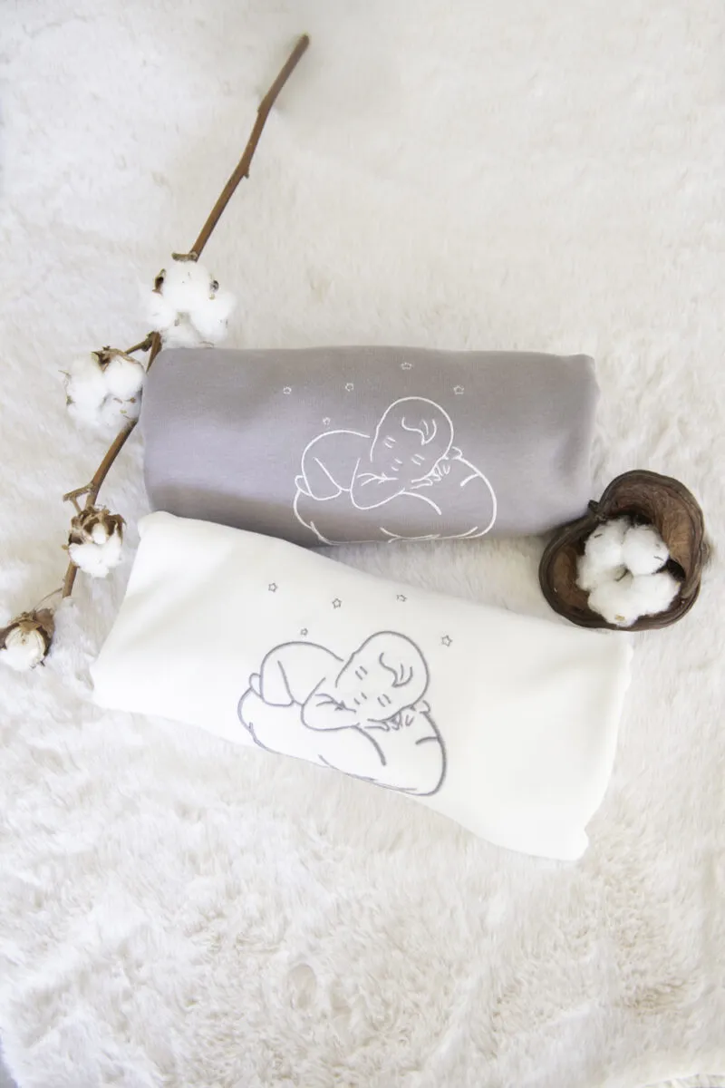 Couvertures bébé en coton bio écrue et grise roulées, avec un doudou