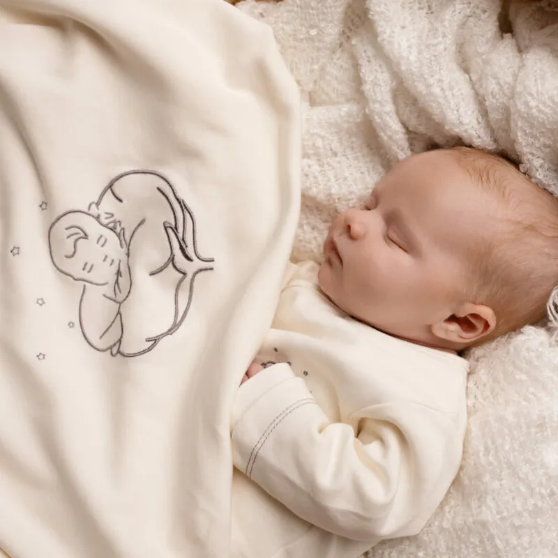 Bébé allongé sur une couverture bébé bio écrue brodée du logo Bébé Coton