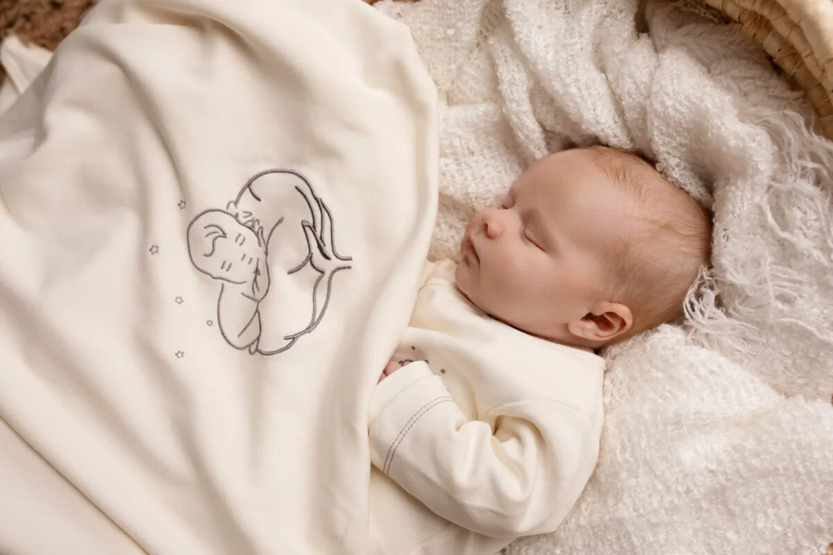Bébé allongé sur une couverture bébé bio écrue brodée du logo Bébé Coton
