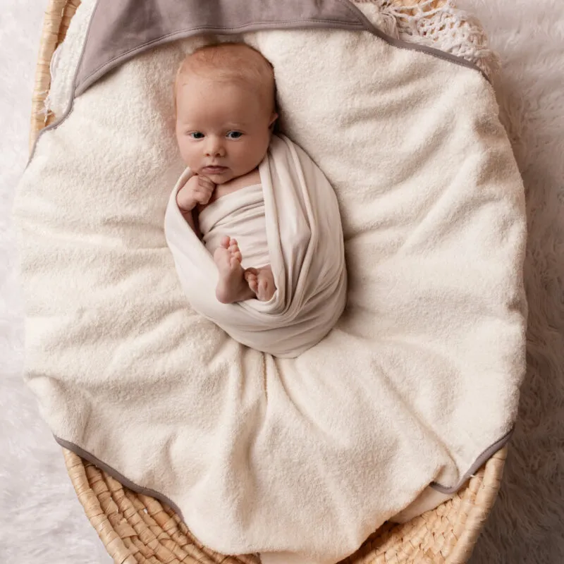 Bébé dans un couffin, enveloppé dans une sortie de bain bébé en coton bio