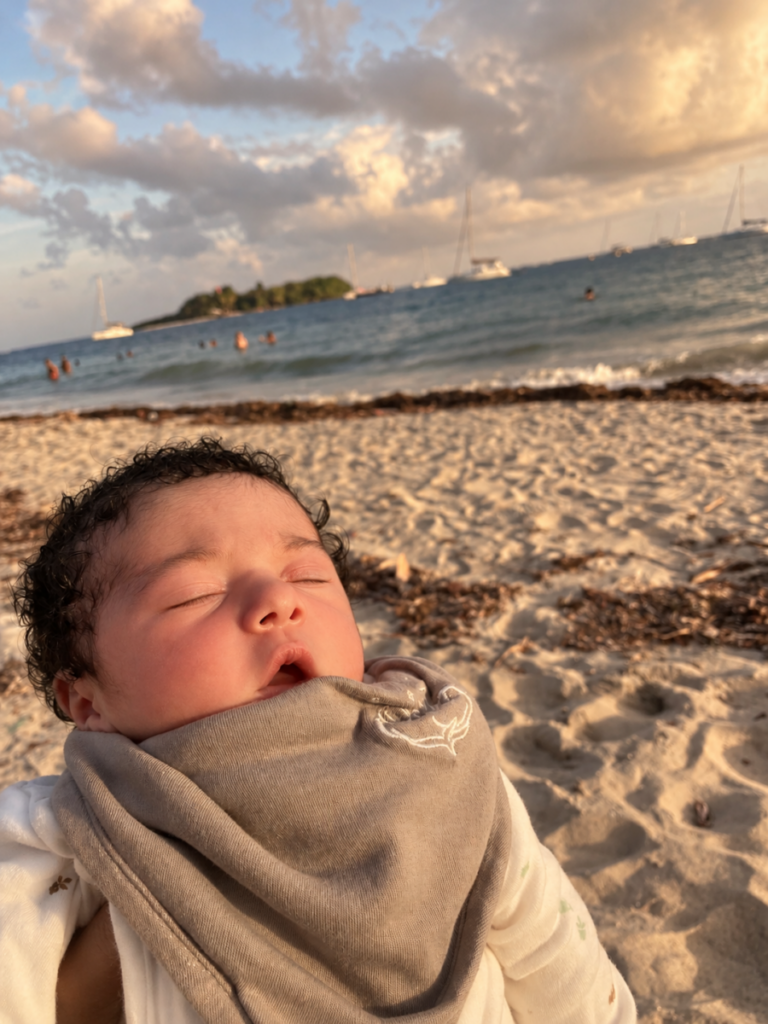 Bébé endormi sur la plage au coucher du soleil, emmailloté dans un lange taupe Bébé Coton en coton bio