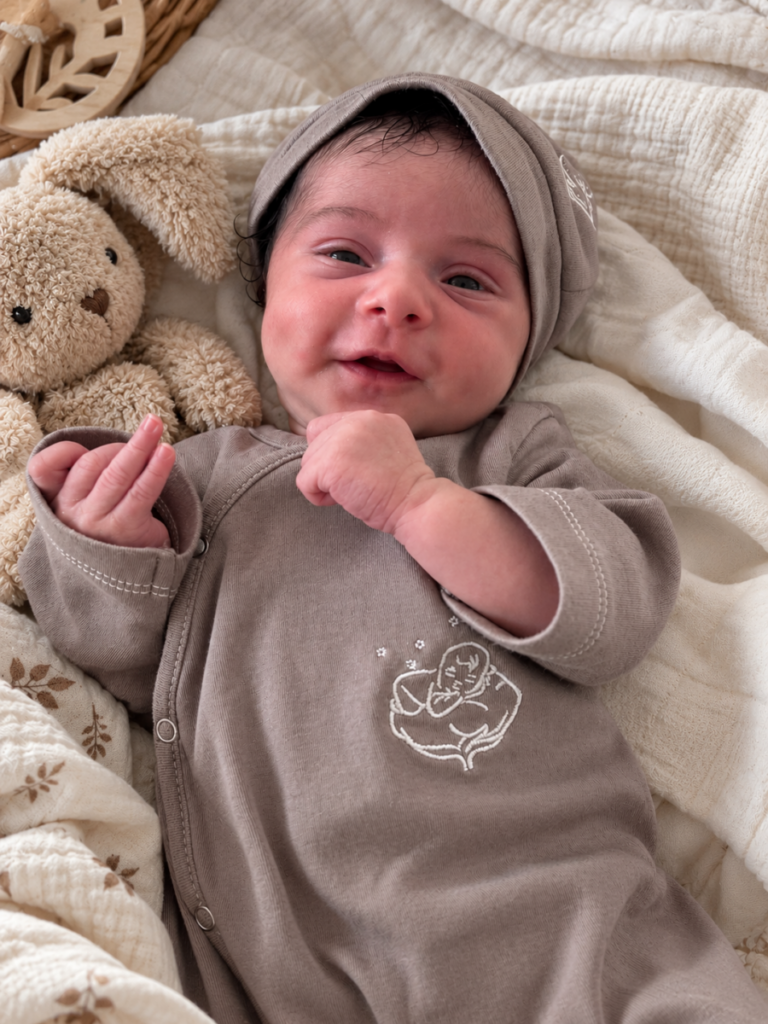 Nouveau-né souriant en pyjama et bonnet taupe Bébé Coton en coton bio, avec son doudou