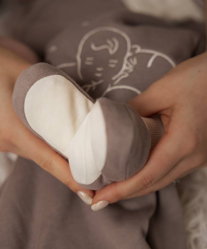 Chaussons bébé en coton bio gris et écru tenus dans les mains, pour vous contacter chez Bébé Coton